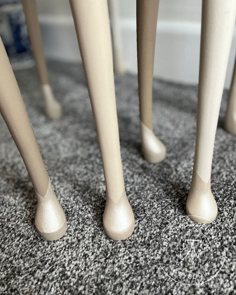 Close-up view of the legs of a set of nesting tables that have been upcycled and painted in neutrals with V-shaped detail on the feet