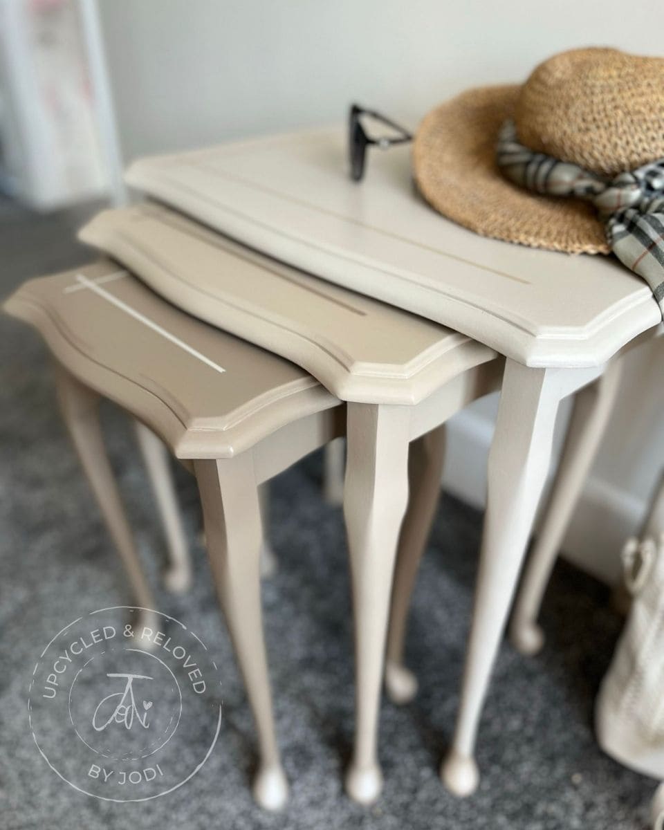 Set of three upcycled nesting tables painted in natural neutrals with decorative items on top, featuring 'Upcycled & Reloved by Jodi' branding