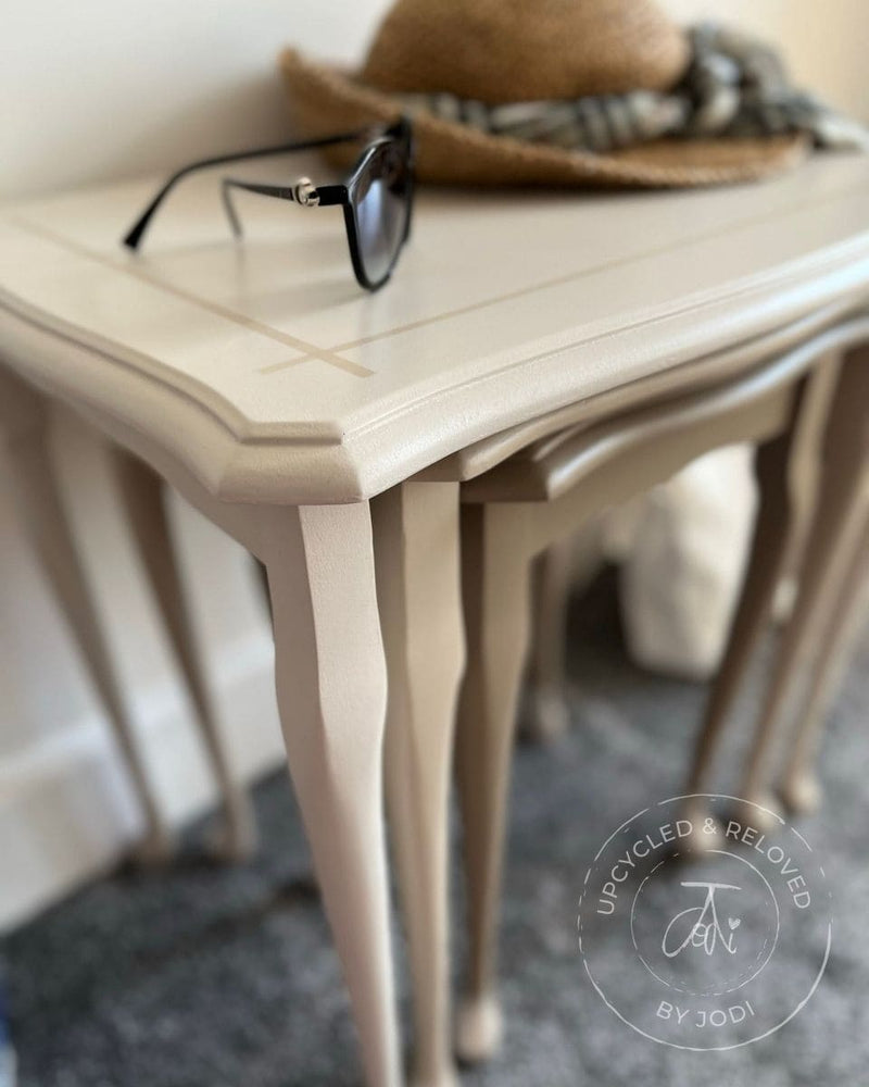 Close-up of upcycled nest of tables painted in neutrals with sunglasses and a sun hat 