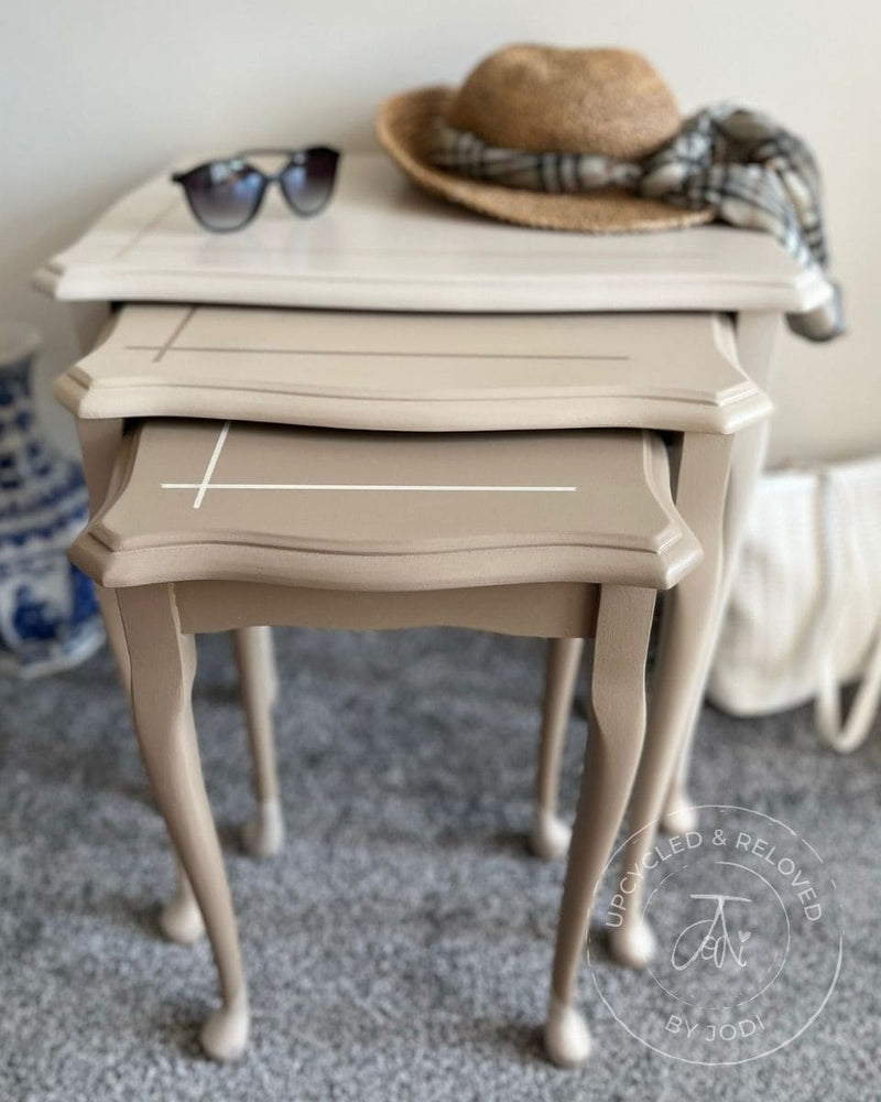 Upcycled nest of tables painted in natural neutrals with sunglasses and a sun hat on top, featuring 'Upcycled & Reloved by Jodi' branding