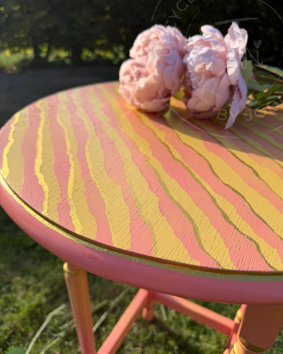 the round top of a colourful striped coral and yello hsand painted upcycled side table. Gold trim is visible on the jagged stripes and round the rim