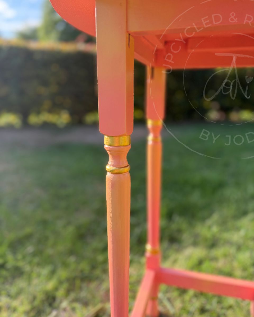 A colourful upcycled hand painted table showing gold detail round the carved legs. a coral an yellow paint blend using fusion paint
