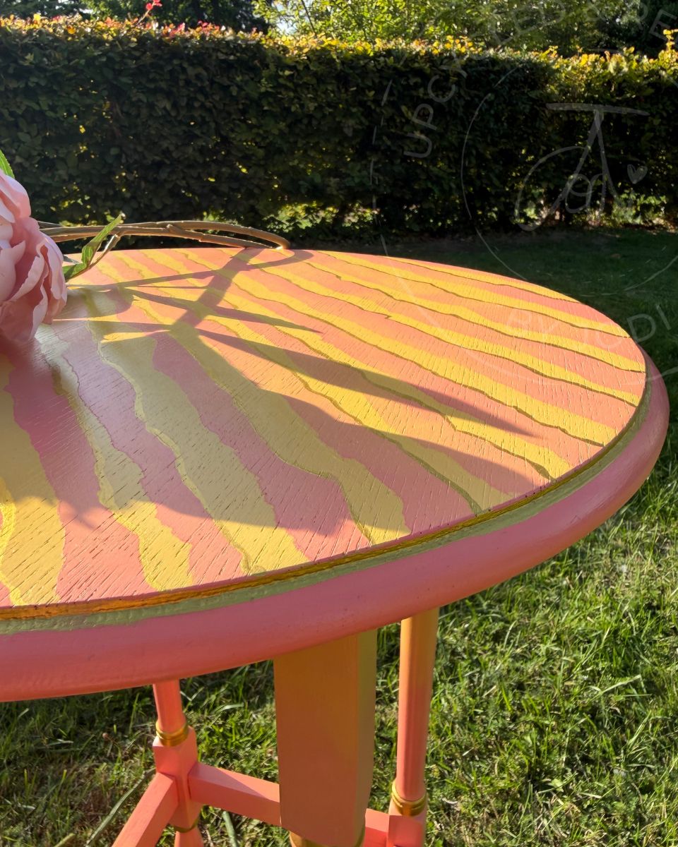 a partial view of painted round side table, the top has coral and yellow zebra striped pattern with touches of gold and a gold fine line around the rim. the log "Upcycled & Reloved by JOdi" is visible