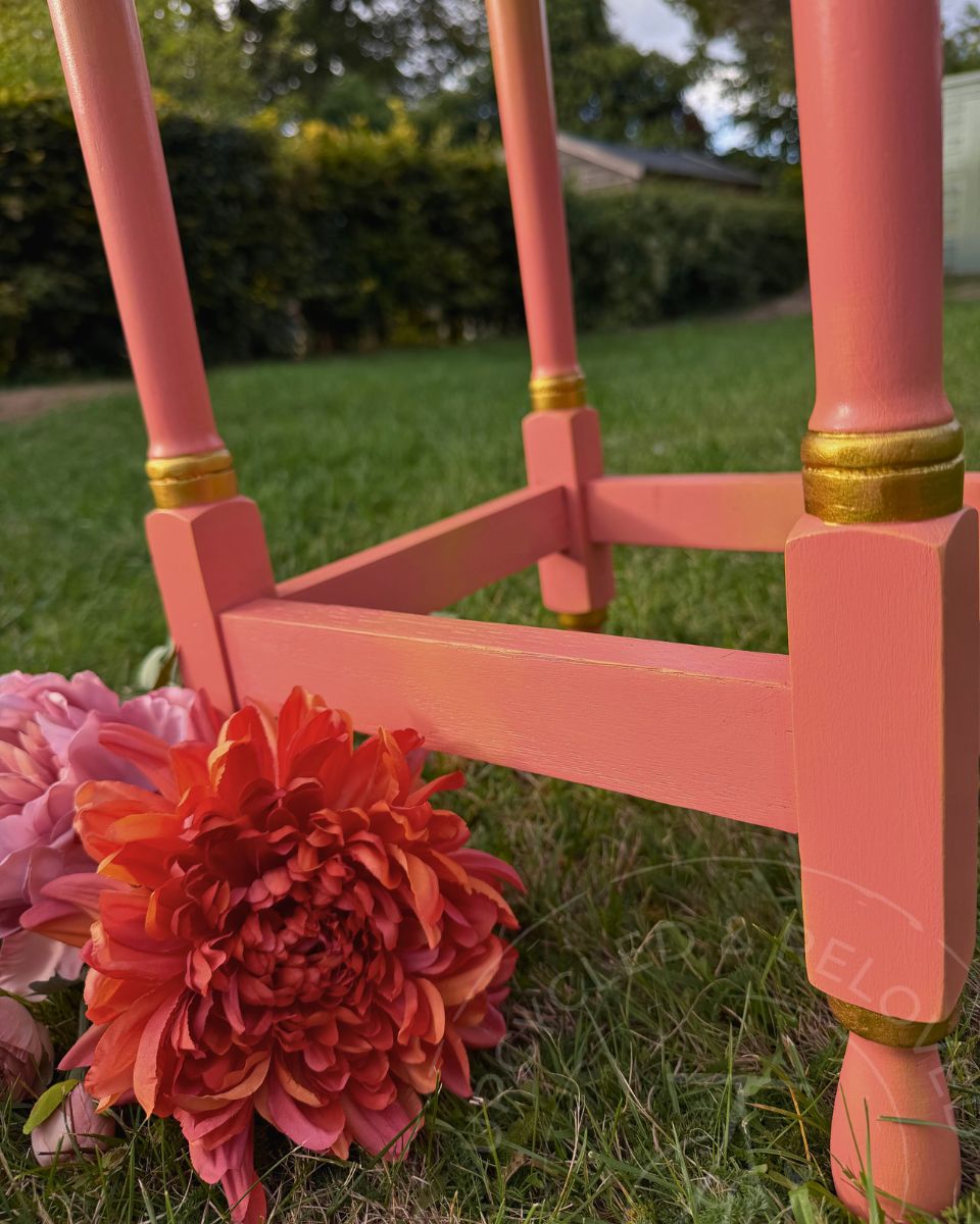 The carved legs and base of a side table upcycled and painted in coral pink with gold detail on the legs