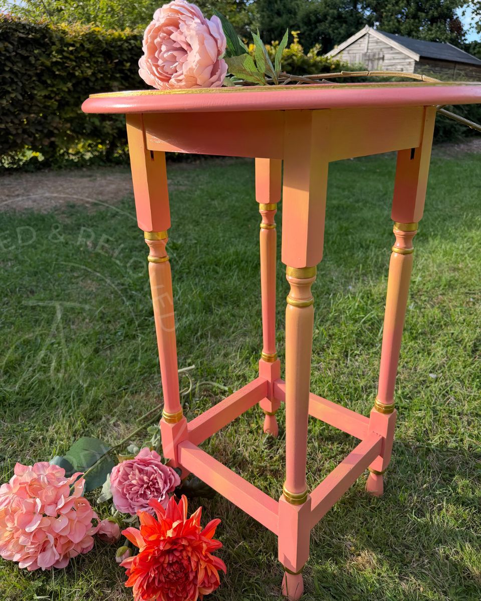 a circular coral painted upcycled vintage side table with yellow and gold details on the legs