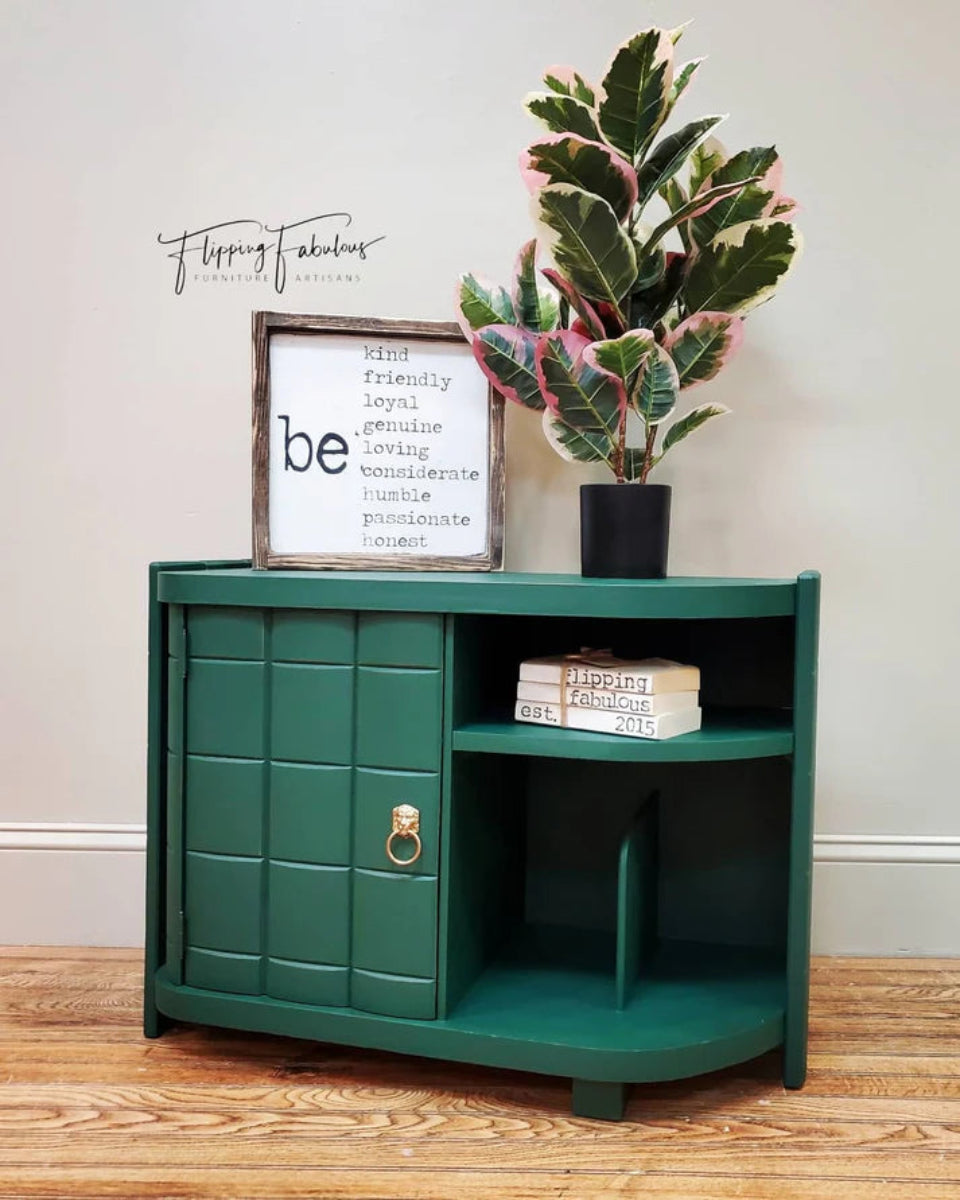 Cabinet with a plant, books, and a framed quote on a wooden floor.