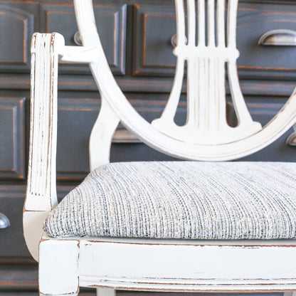 Chair painted in Raw Silk Fusion Mineral Paint with gray cushion in front of a dark wooden cabinet.