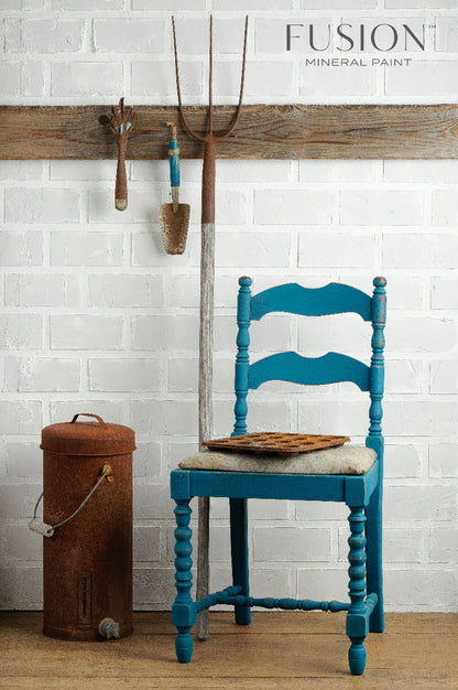 Wooden chair painted in Renfrew Blue from the Fusion Mineral Paint range against a white brick wall