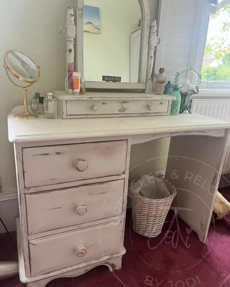 A distressed white wooden dressing table with three drawers and a matching mirror before being restyled by Upcycled & Reloved by Jodi in Surrey, UK to match a green and cream chest of drawers.