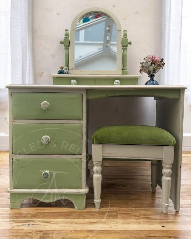 A shabby chic dressing table set with a three-drawer cabinet, an arched mirror, and a matching stool, painted in Upper Canada Green and Champlain from Fusion Mineral Paint range with decorative knobs, set on a wooden floor.