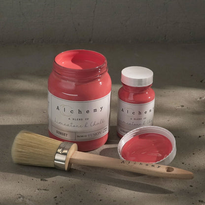 Jars of vibrant coral-coloured Sunset paint from Alchemy by Fusion against a plain textured background