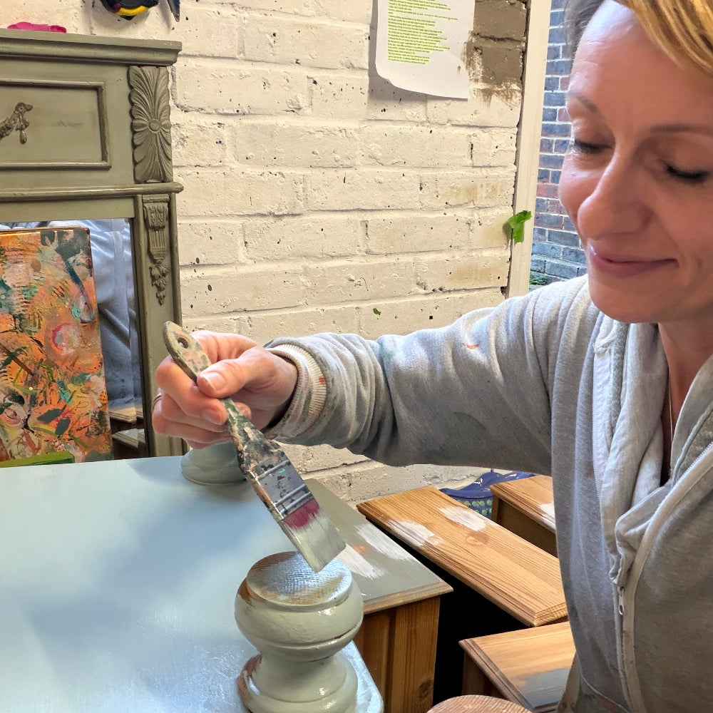 Jodi from Upcycled and Reloved by Jodi applying paint to a wooden bedside table in her upcycling workshop