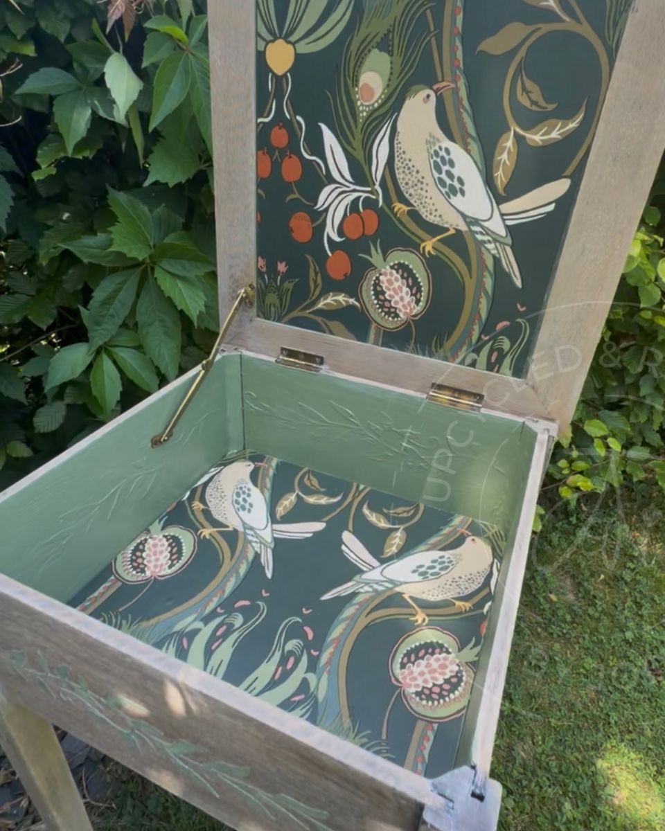 An upcycled sewing box storage side table showing an open lid with a patterned bird and leafy decoupage print on the underside and bottom. The inside is painted in pale green with a raised leafy detail