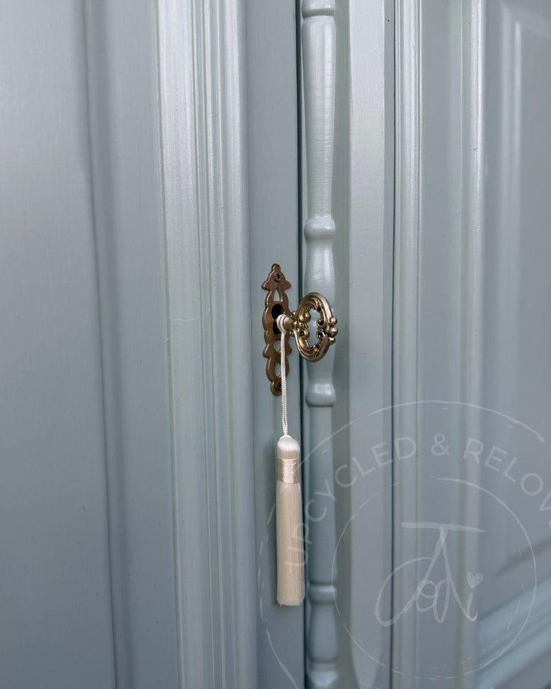 Close up of gold gilded key and lock, with a white tassel, on a Welsh dresser cupboard door upcycled by Upcycled & Reloved by Jodi in soft blue-green Fusion Mineral Paint Inglenook.