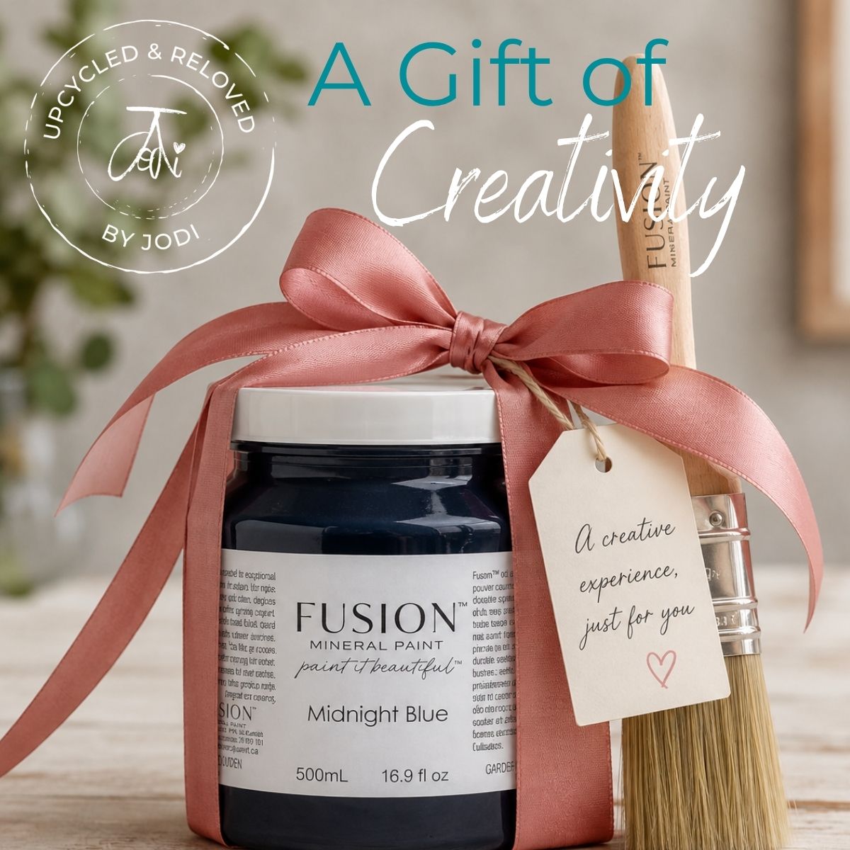 A gift voucher for furniture upcycling, gift cards for creatives, unusual gift card ideas, unique gift voucher, shows a jar of fusion mineral paint as a gift with a ribbon and gift label and a furniture paint brush leaning against the jar,. The title read 'A Gift Of Creativity' Gift vouchers available in Surrey